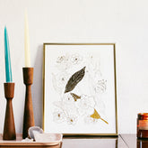 Photo of a Botanical art print with floral pattern in gold foil in a gold frame next to candles